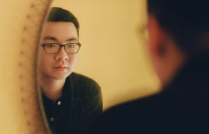 Asian man looking into the mirror, potentially not being a best friend to himself