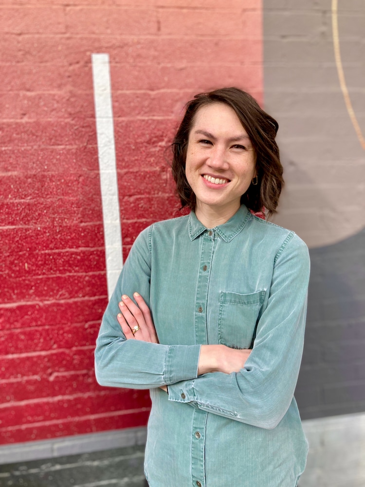 Photograph of Miranda Nadeau, Ph.D. standing against a mural